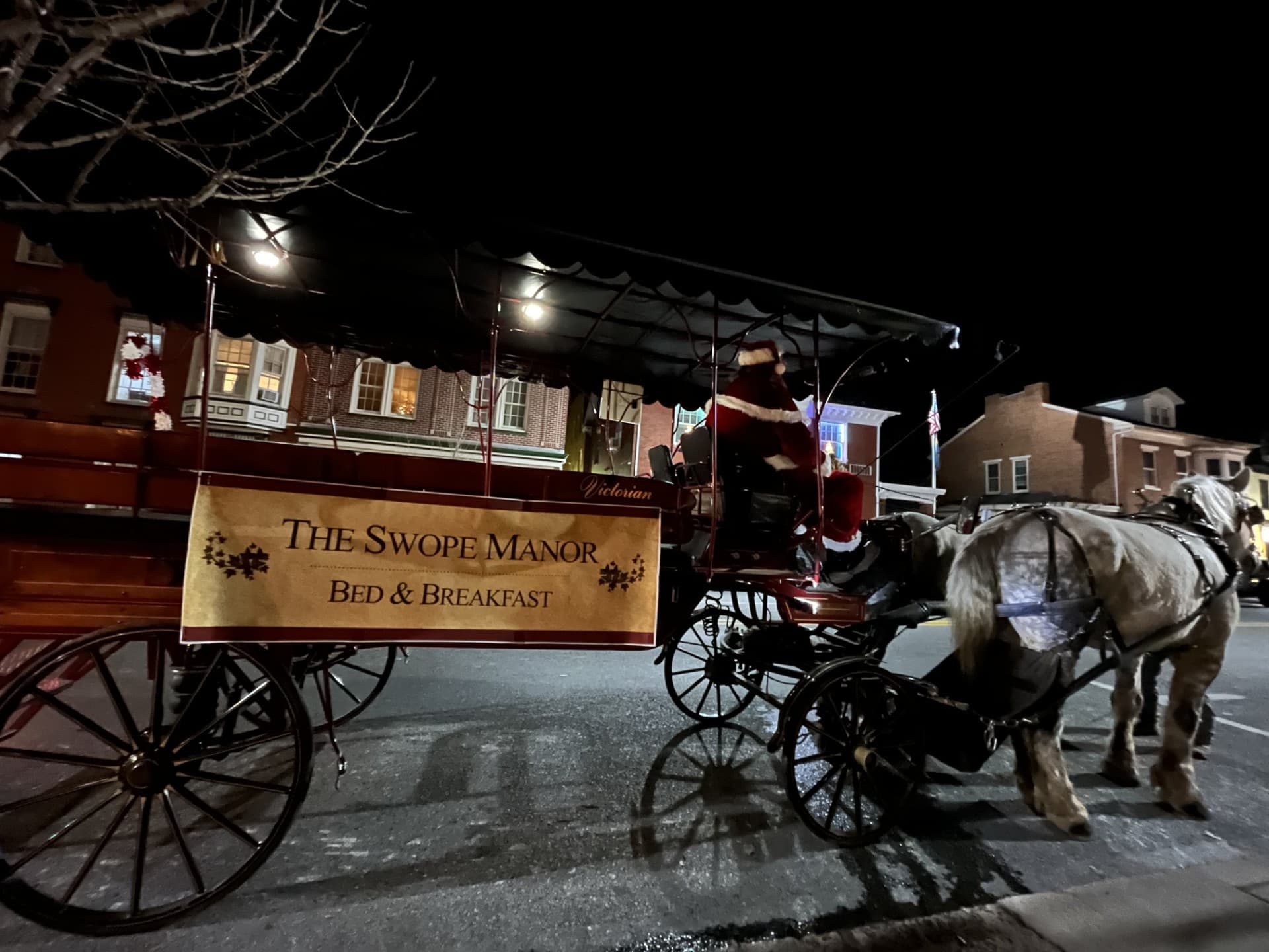 A festive horse-drawn carriage with a "Swope Manor Bed & Breakfast" sign is parked on a street at night.