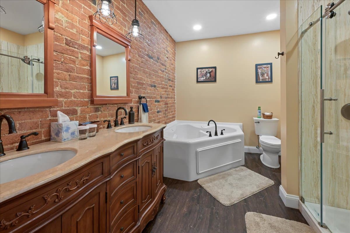 A modern bathroom featuring a double vanity, a freestanding bathtub, and exposed brick walls.