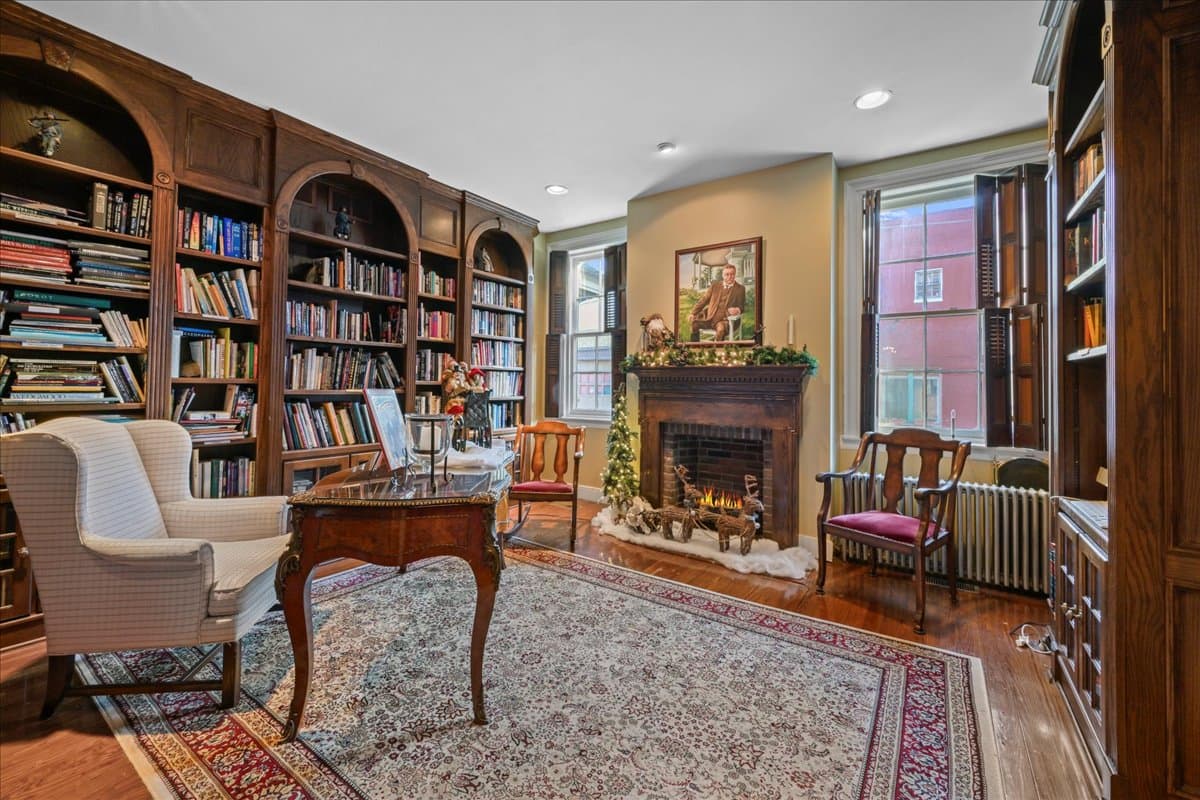 Cozy library with bookshelves, a fireplace, and comfortable seating.